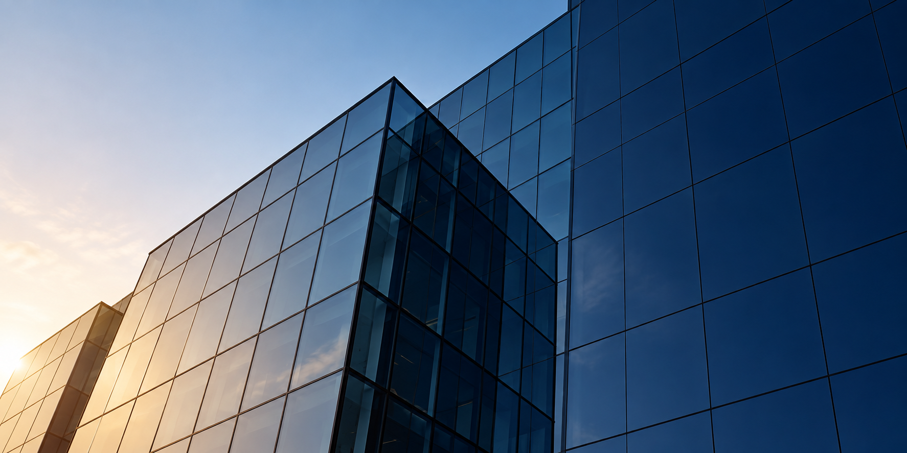 Modern glass architecture reflecting warm sunlight and a blue sky.